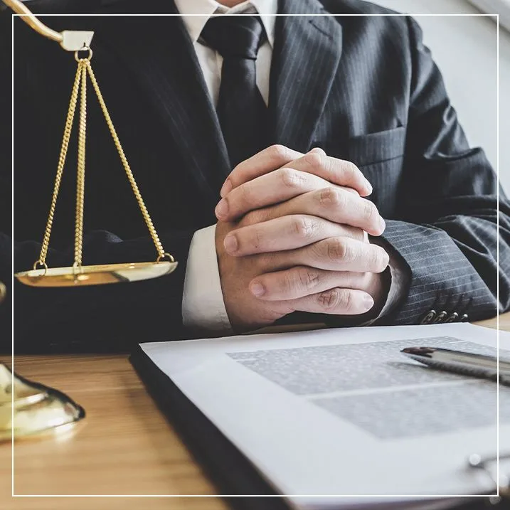 lawyer with their hands together at a desk with a scale and paper work in front of them